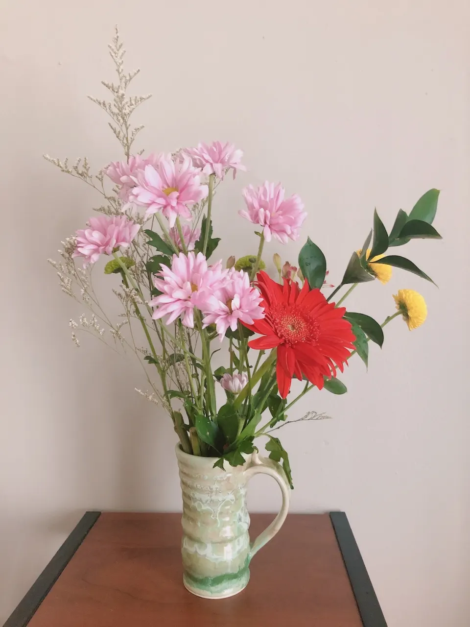 Pink, red, and yellow flowers arranged in a ceramic pitcher